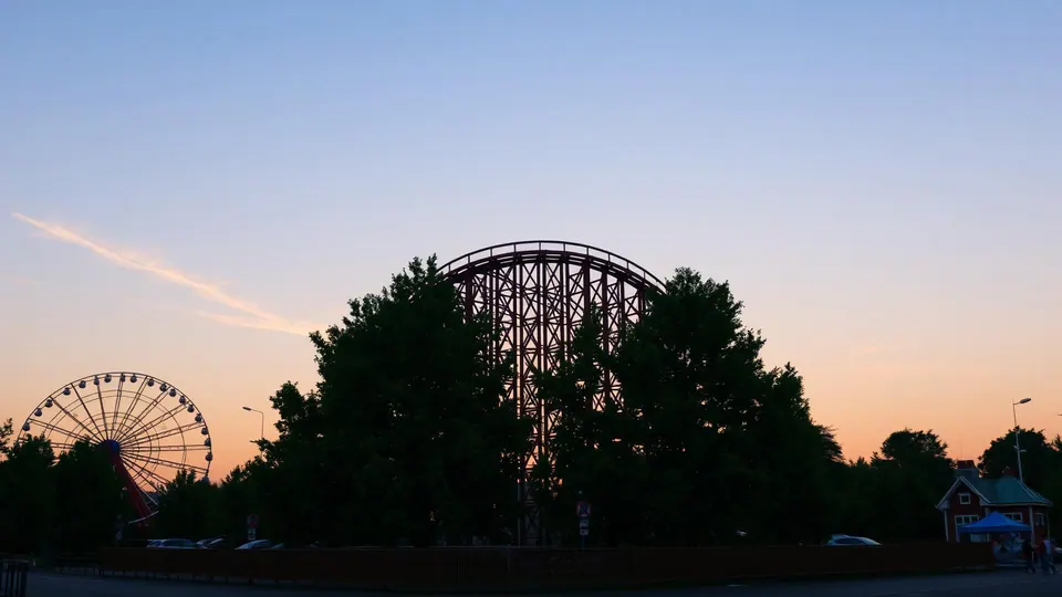 Holzachterbahn und Riesenrad eines Familien-Freizeitparks im Norden bei Sonnenuntergang, Bäume im Vordergrund