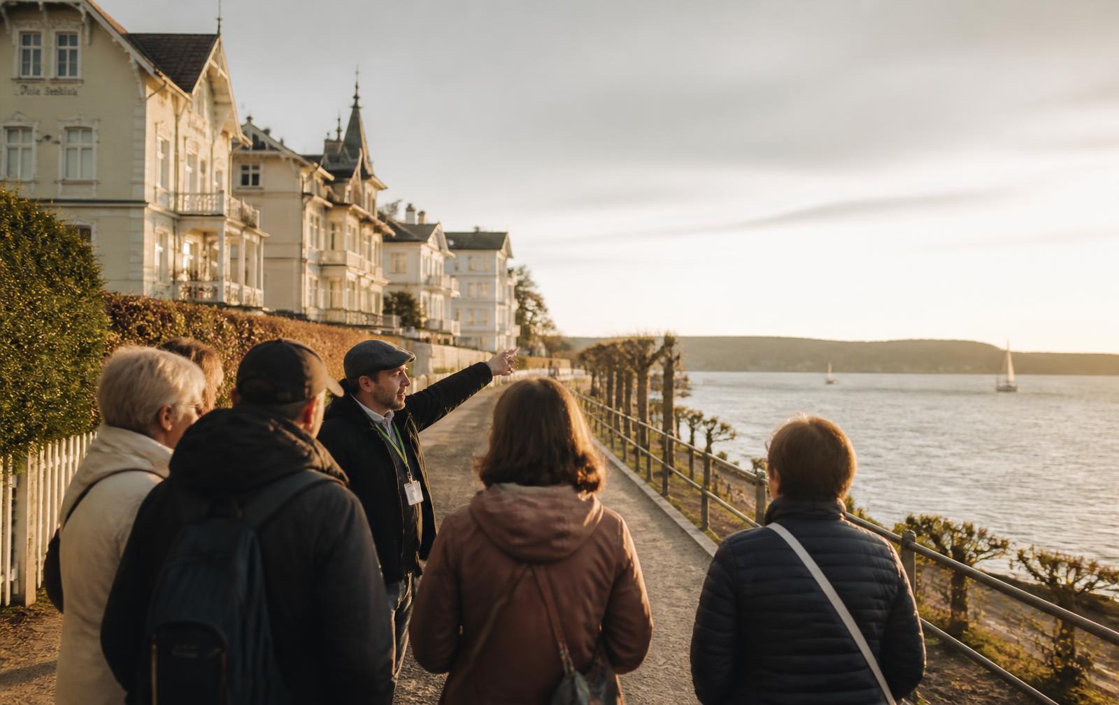 Kleine Gruppe bei einer geführten Tour auf der Kurstrandpromenade in Glücksburg mit Blick auf die Flensburger Förde
