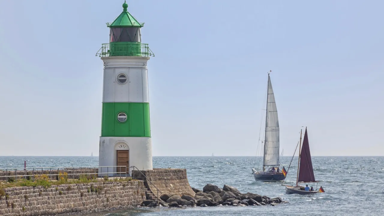 Leuchtturm Schleimünde — grün-weiß gestreifter Turm von 1871 auf der Lotseninsel mit zwei Segelbooten auf der Ostsee