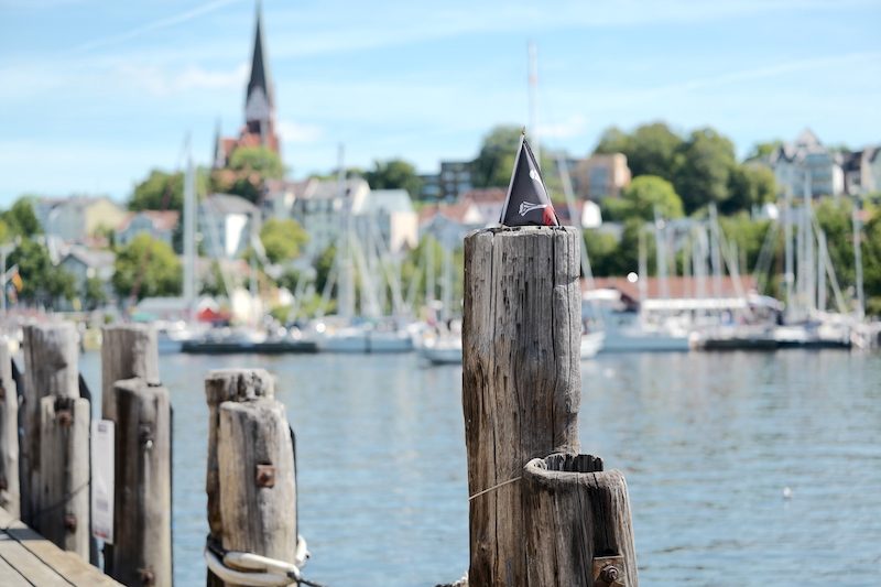 Holzdalben am Flensburger Hafen mit Kirchturm im Hintergrund
