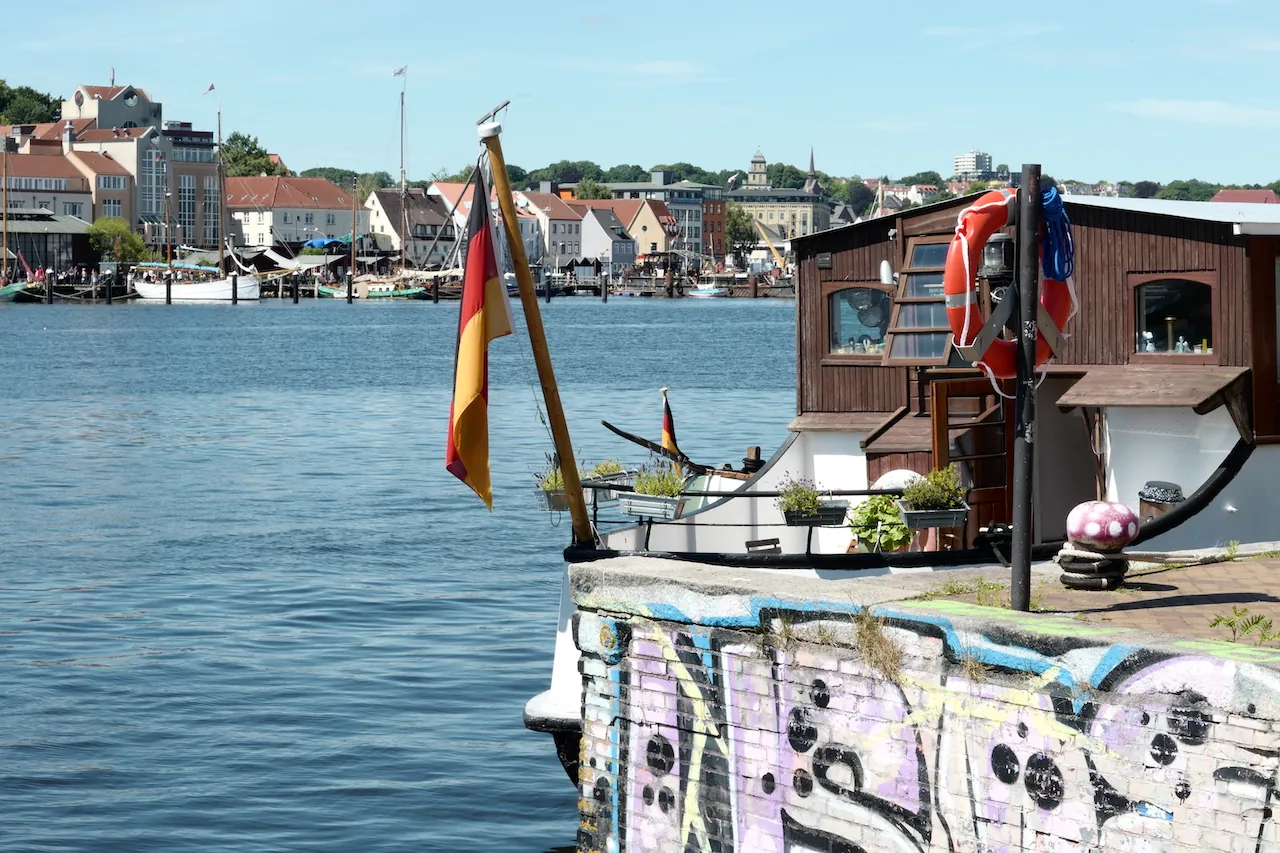 Buntes Hausboot im Flensburger Hafen mit Stadtkulisse