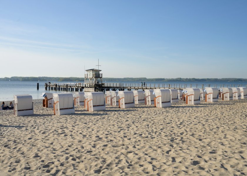 Weiße Strandkörbe am Sandstrand von Glücksburg mit Seebrücke